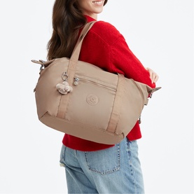 Model carrying a large beige nylon tote bag with front zip pocket, top handles, and signature Kipling monkey keychain, styled with a red jumper.