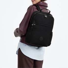 Model carrying a large black nylon backpack with multiple zip compartments and silver-tone hardware, styled with a light blue shirt and burgundy