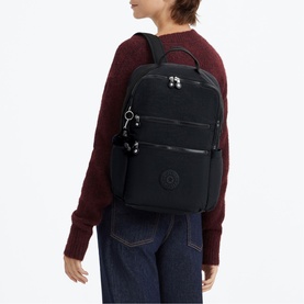 Model carrying a large black Kipling backpack with silver hardware, multiple zip compartments, and top carry handle, styled with a burgundy knit