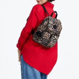 Model carrying Kipling backpack in Wild Leopard print with black straps and hardware, styled with red shirt and blue jeans.