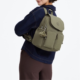 Model carrying olive green nylon backpack with flap closure, monkey keychain charm, worn with denim jacket and brown trousers