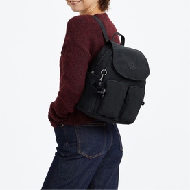 Model carrying black Kipling backpack with front pockets and keychain charm, styled with burgundy sweater and jeans