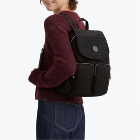 Model carrying a black textured backpack with flap closure, zip pockets, and dark hardware, styled with a burgundy sweatshirt and jeans