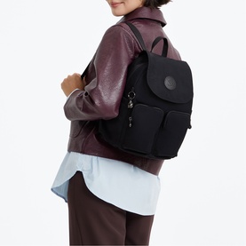Model carrying a black nylon backpack with front pockets and dark hardware, styled with a burgundy jacket and white shirt.