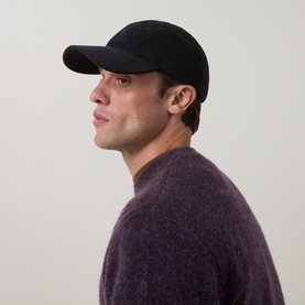 Model with Calvin Klein Monogram Logo Corduroy Cap in black, curved visor, six-panel construction, styled with purple crew-neck jumper