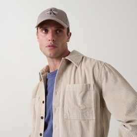 Model with Calvin Klein Monogram Logo Cap in Fur Moon Rock, curved visor, embroidered monogram detail, styled with striped overshirt
