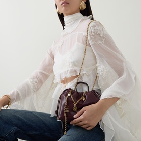 Model carrying Chloe Icons Leather Mini Crossbody Bag in Burnt Red with gold chain strap, styled with white lace blouse and jeans