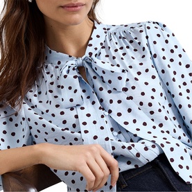 Model wearing Phase Eight blue polka dot blouse with bow neckline, puff sleeves, and ruffle front detail