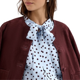 Model wearing Phase Eight blue polka dot pussy-bow blouse, styled with a dark burgundy jacket. Close-up shot showing neckline detail.