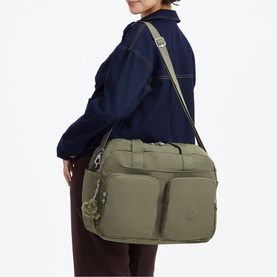 Model carrying Kipling bag in Almost Sage green nylon, worn crossbody with gold-tone zip pulls and front pocket detail.