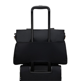 Black tote bag with luggage sleeve slotted onto black rolling suitcase handle, gold-tone hardware detail visible