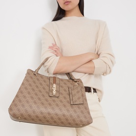 Model carrying Guess Latte Logo tote bag with gold-tone hardware and luggage tag, styled with cream sweater and matching trousers