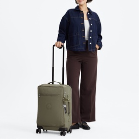 Model carrying an olive green soft-shell cabin suitcase with extended handle and four spinner wheels, styled with denim jacket and wide-leg trousers