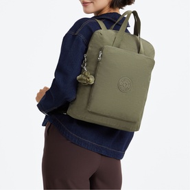 Model carrying Kipling backpack in Almost Sage green, worn on back, with zip front pocket and monkey keychain charm.