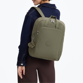 Model carrying sage green Kipling backpack with zip pockets, monkey keychain charm, and adjustable shoulder straps, styled with denim jacket