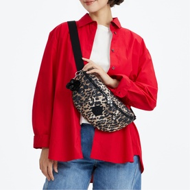 Model carrying leopard print belt bag with black crossbody strap, worn over red oversized shirt and blue jeans