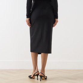 Model wearing Max Mara Studio nero wool midi skirt, rear view, styled with black long-sleeve top and black strappy heels.