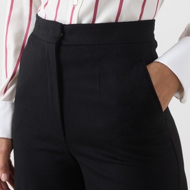 Model wearing Max Mara Studio black wool trousers, high-waisted with side pockets, styled with a white striped shirt.