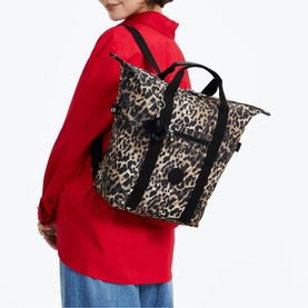 Model carrying leopard print tote backpack with black straps and hardware, styled with red jacket and blue jeans