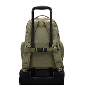 Olive green canvas backpack shown from rear, with padded straps and luggage sleeve, mounted on a black rolling suitcase
