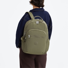 Model carrying Kipling backpack in Almost Sage green nylon with silver-tone hardware, small monkey keychain, styled with navy jacket and burgundy