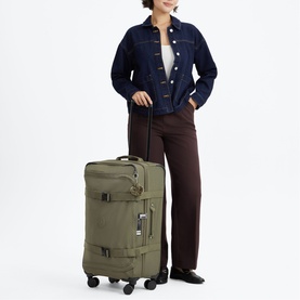 Model carrying Kipling Almost Sage large soft-shell suitcase on wheels with top handle, styled with denim jacket and wide-leg trousers.