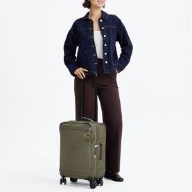 Model carrying a khaki green soft-shell cabin suitcase with spinner wheels, styled with a navy denim jacket and brown wide-leg trousers.