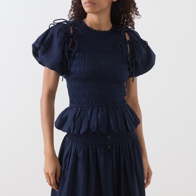 Model wearing Damson Madder Navy Blouse in cotton with puff sleeves, smocked bodice and tie details, styled with matching navy skirt.