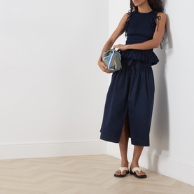 Model wearing Damson Madder navy cotton blouse with matching midi skirt, styled with a blue mini bag and tan flat sandals.
