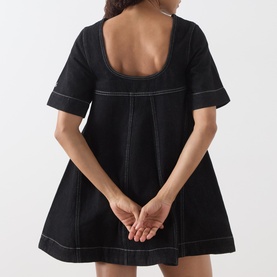 Model wearing Damson Madder black mini dress, back view showing square neckline, short sleeves, A-line skirt and contrast white stitching detail.