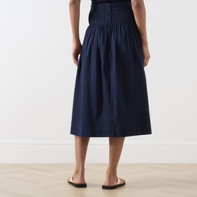 Model wearing Damson Madder navy cotton midi skirt with elasticated waist and pleated detail, styled with black top and sandals.