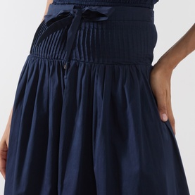 Model wearing Damson Madder navy cotton skirt with smocked waistband, tie detail, and gathered full skirt.