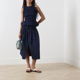 Model wearing Damson Madder navy cotton midi skirt with front split, styled with matching top, small iridescent bag and white sandals.