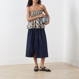 Model wearing Damson Madder Cardamon Check cotton top, styled with navy midi skirt and black embellished flat mules.