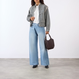 Model wearing FRAME DENIM Dodger Wide Leg jeans in light blue, styled with a grey jacket, white shirt and dark tote bag.