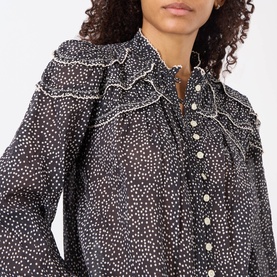 Model wearing Isabel Marant Etoile black and ecru cotton top with ruffle bib collar, white dot print, and pearl button fastening.