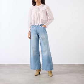 Model wearing Isabel Marant Etoile light pink cotton blouse with ruffle detail, styled with wide-leg light blue jeans and beige ankle boots.