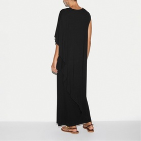 Model wearing Jigsaw black maxi dress with asymmetric cape sleeve, styled with tan flat sandals, back view