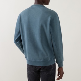 Model wearing Belstaff petrol blue cotton sweatshirt, rear view, ribbed cuffs and hem, styled with dark jeans