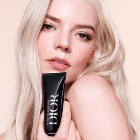 Model with Dior Forever Skin Veil Makeup Primer, holding black tube product close to face, platinum blonde hair, natural makeup look