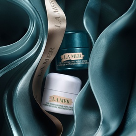 La Mer Day & Night Routine Travel Gift Set featuring two cream jars in teal and white packaging, styled on draped silk fabric with ribbon.