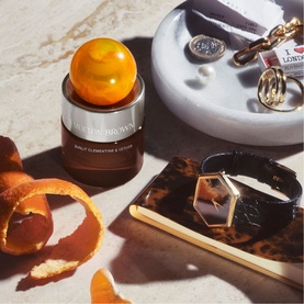 Molton Brown Sunlit Clementine & Vetiver 30ml EDP bottle with amber sphere cap, styled with jewellery and accessories on marble surface.