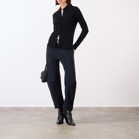 Model wearing Nili Lotan navy cotton trousers with relaxed fit, styled with black zip-up top, small clutch bag and black ankle boots.