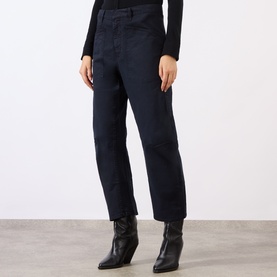 Model wearing Nili Lotan navy cotton trousers with a relaxed tapered leg, styled with a black top and black heeled ankle boots.