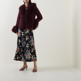 Model wearing Rixo London maroon lamb suede jacket with fluffy fur trim collar and cuffs, styled with black floral midi skirt and heeled sandals.