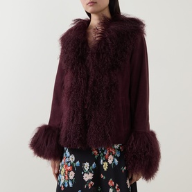 Model wearing Rixo London maroon lamb suede jacket with fluffy shearling trim collar and cuffs, styled with a floral skirt.