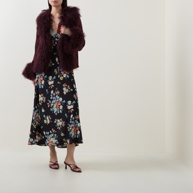 Model wearing Rixo London maroon lamb suede jacket with fluffy faux fur trim, styled with a black floral midi dress and strappy heels.