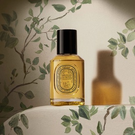 Diptyque Body Oil in amber glass bottle with black cap, featuring signature circular label, styled with botanical backdrop