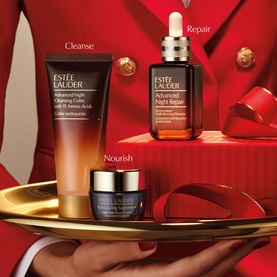 Est&eacute;e Lauder Advanced Night Repair Skincare Gift Set with serum, cleansing gel and eye cream on gold tray with red ribbon backdrop.