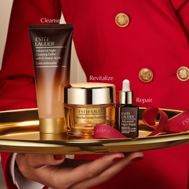 Est&eacute;e Lauder Revitalizing Supreme+ Skincare Gift Set with cleanser, moisturiser and night repair serum on gold tray, held by model in red jacket.